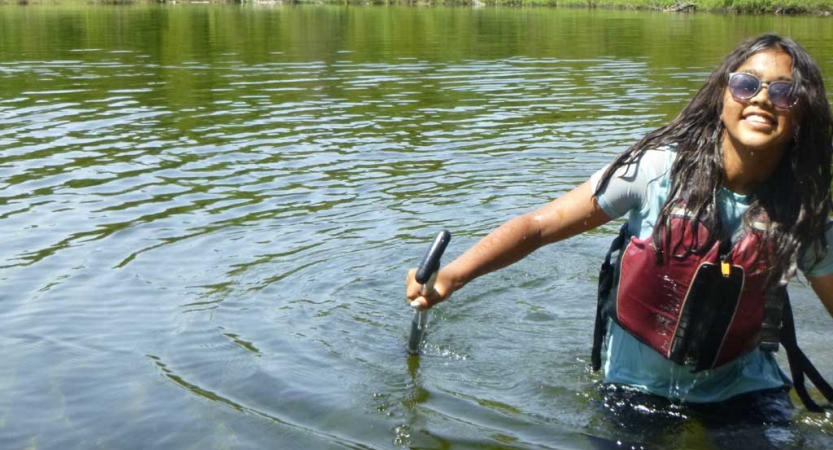 A person wearing a life jackets stands in waist-deep water and smiles